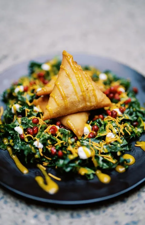 A Foodz dish with golden pastry, greens, and pomegranate on a blue plate